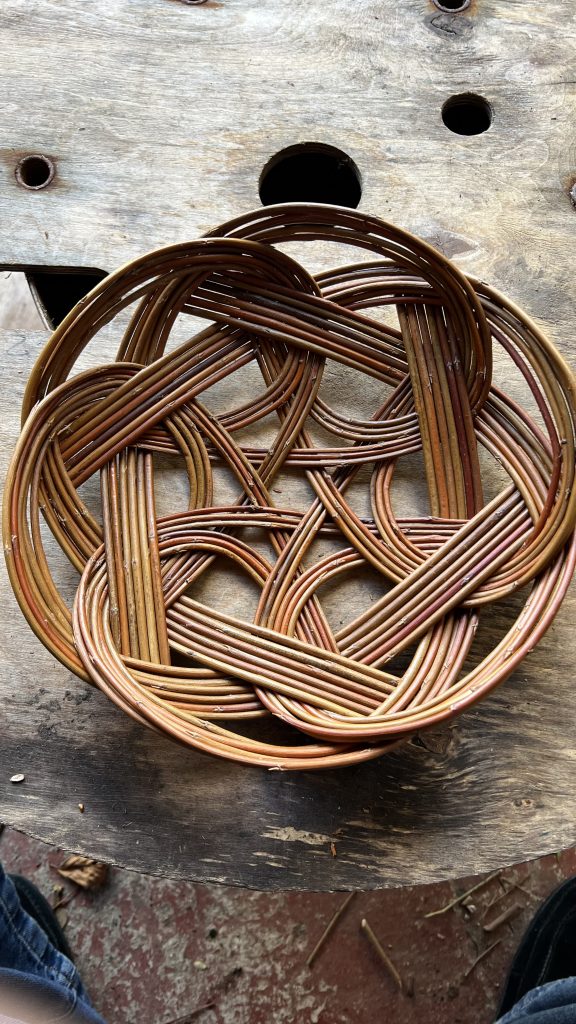 A round bread basket woven in red willow on a wooden background.